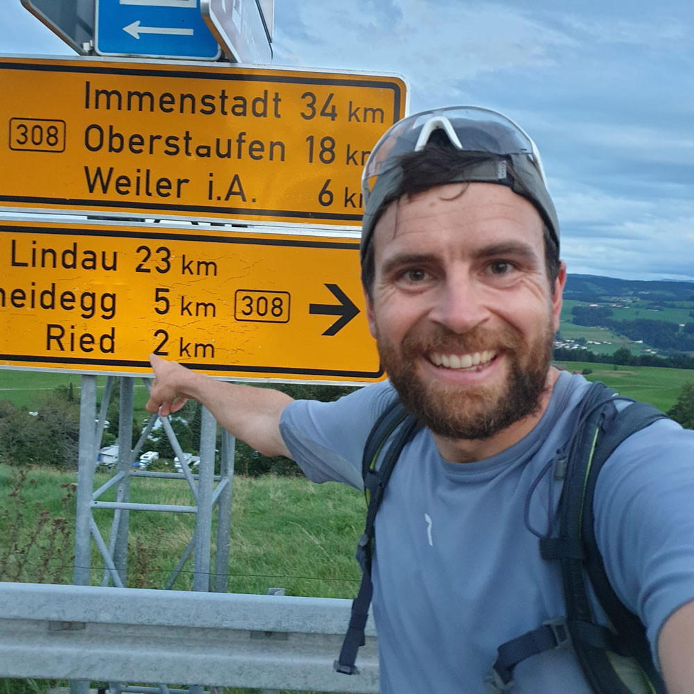 Jonas Deichmann vorm Straßenschild Richtung Lindau
